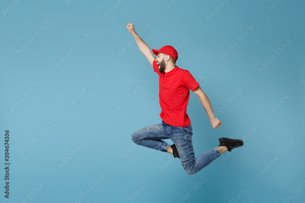 Delivery man in red uniform workwear isolated on blue wall background, studio portrait. Professional male employee in cap t-shirt print working as courier dealer. Service concept. Mock up copy space. Delivery man in red uniform workwear isolated on blue wall background, studio portrait. Professional male employee in cap t-shirt print working as courier dealer. Service concept. Mock up copy space.