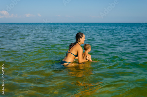 A young mother in a swimsuit plays with her young son in the sea.