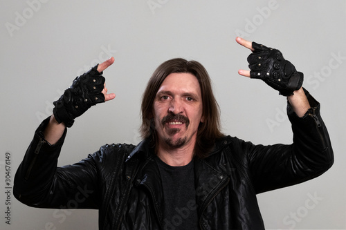 Adult rock fan makes corna gesture. Portrait of a long-haired man in a black jacket and fingerless gloves. A guy who looks like a Mexican biker or heavy metal musician.