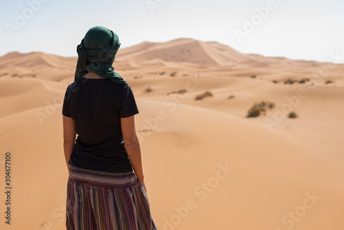 Woman looking at the horizon dunes in the Moroccan Sahara desert.