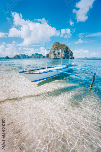 El Nido, Palawan, Philippines. Banca boat on sandy beach in shallow crystal clear water on island hopping trip. Amazing Pinagbuyutan island in background. Beautiful landscape scenery photo