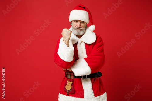 Angry elderly gray-haired mustache bearded Santa man in Christmas hat posing isolated on red background in studio. Happy New Year 2020 celebration holiday concept. Mock up copy space. Clenching fist.