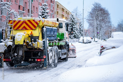  Snow plow service truck removing snow and gritter spreading salt on the city housing estate road.