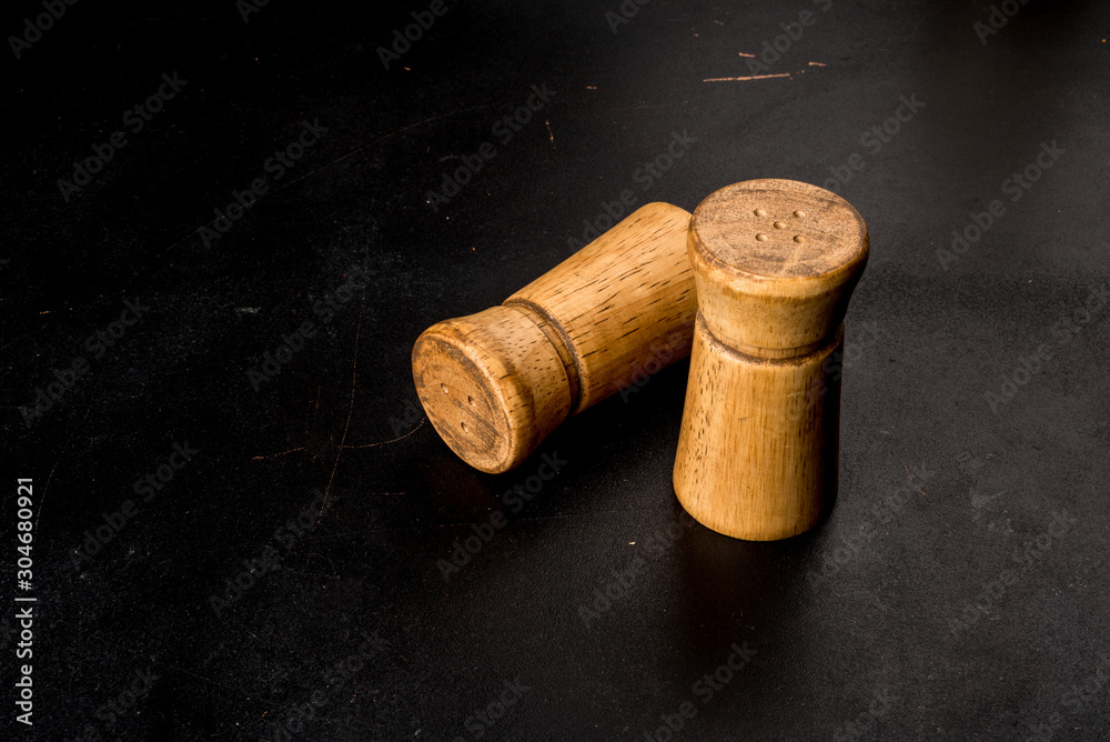Salt and pepper in wooden salt shakers on a black background