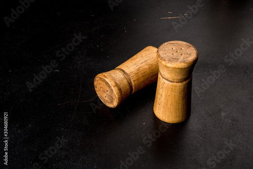 Salt and pepper in wooden salt shakers on a black background