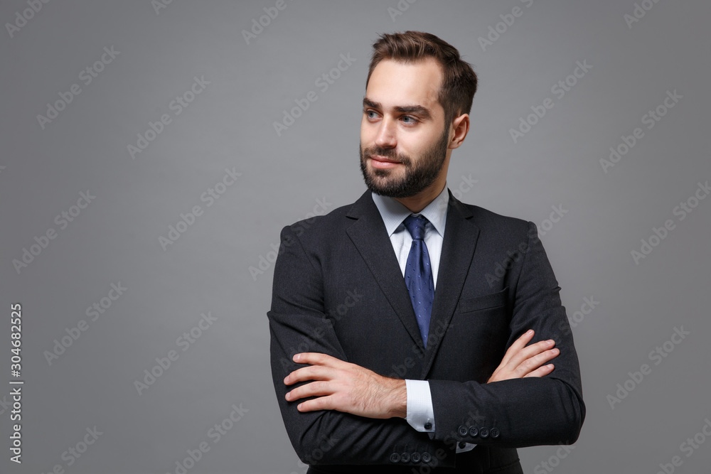 Handsome young business man in classic black suit shirt tie posing isolated on grey background. Achievement career wealth business concept. Mock up copy space. Holding hands crossed, looking aside. - obrazy, fototapety, plakaty 