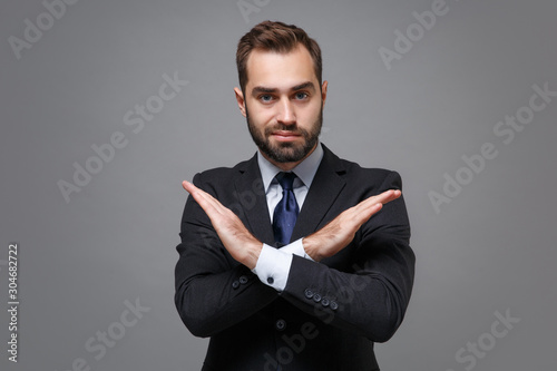 Young bearded business man in classic black suit shirt tie posing isolated on grey background. Achievement career wealth business concept. Mock up copy space. Showing stop gesture with crossed hands.