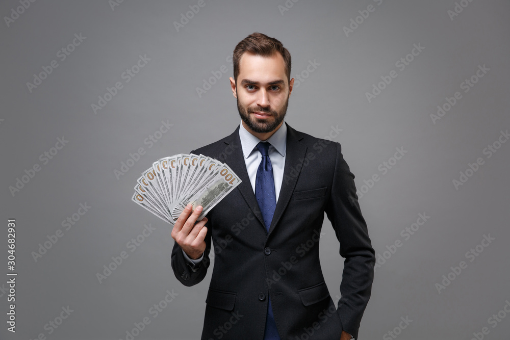 Confident young business man in classic suit shirt tie posing isolated on grey background. Achievement career wealth business concept. Mock up copy space. Hold fan of cash money in dollar banknotes. Confident young business man in classic suit shirt tie posing isolated on grey background. Achievement career wealth business concept. Mock up copy space. Hold fan of cash money in dollar banknotes.