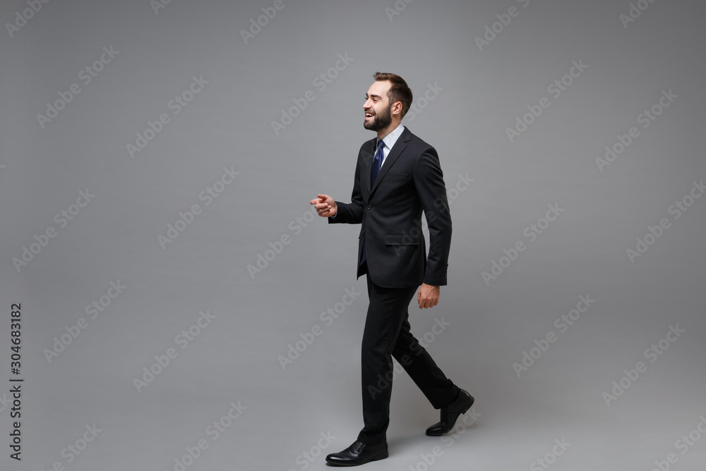 Side view of cheerful young bearded business man in classic black suit shirt tie posing isolated on grey wall background. Achievement career wealth business concept. Mock up copy space. Looking aside. Side view of cheerful young bearded business man in classic black suit shirt tie posing isolated on grey wall background. Achievement career wealth business concept. Mock up copy space. Looking aside.