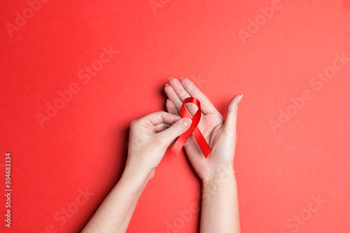 Female hands holding red AIDS awareness ribbon on red background.