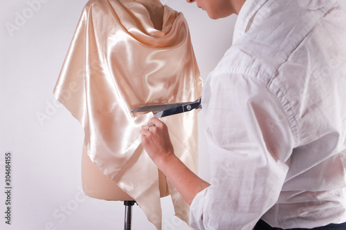 Seamstress cuts fabric with big scissors on a mannequin.