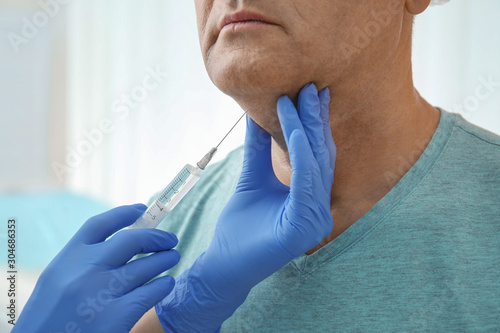 Mature man with double chin receiving injection in clinic, closeup