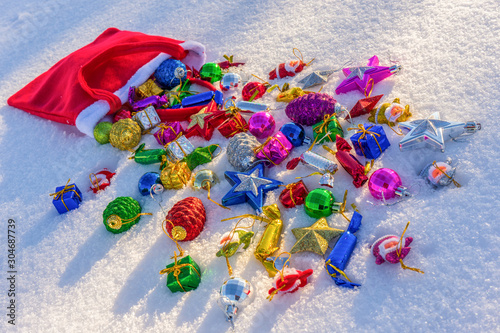 Red bag with many colorful new year toys and decorative items lying on white fresh snow. Santa Claus scattered bag of gifts. Merry Christmas and Happy New Year. Greeting card for winter holidays © Tatyana_Andreyeva