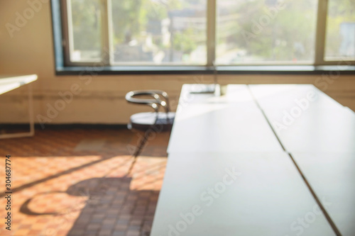Blurred interior of light coworking with large windows  white table  chair and laptop. Unfocused background.