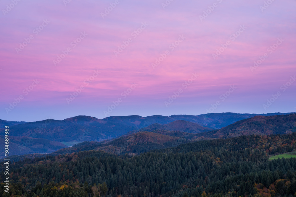 Germany, Endless beautiful natural untouched black forest nature landscape of forest covered hills decorated with red glowing sky after sunset, aerial view above