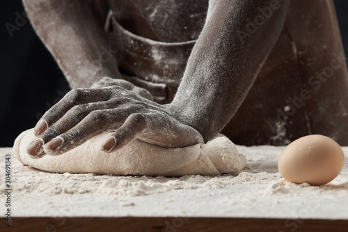 Photography hands of a black man kneading the dough on the table with eggs and flour