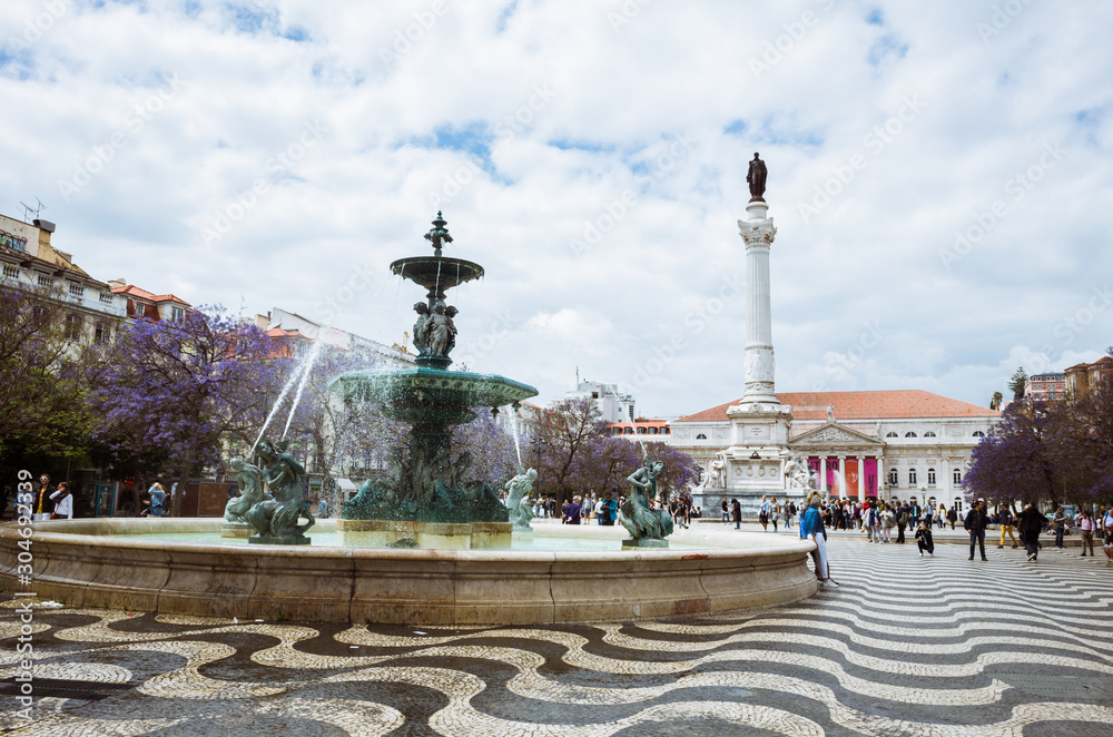 Lisbon, Portugal - May, 28th, 2018 : Rossio square. South fountain, Column of Pedro IV and National theatre in background. Incidental people.