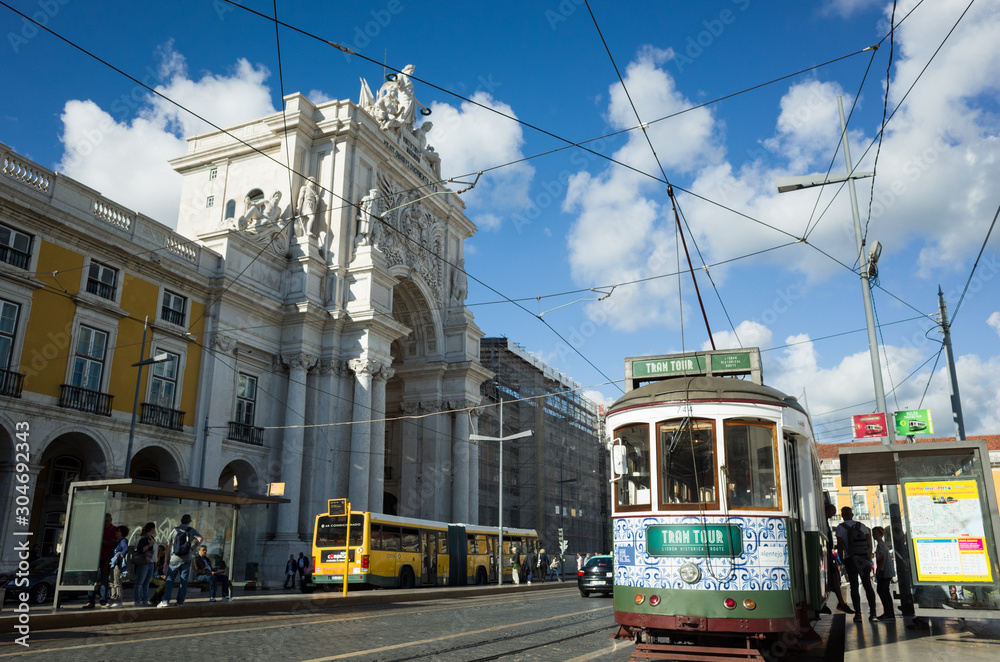 Fototapeta premium Lisbon, Portugal - May, 30th, 2018 : Passengers board an old red tram next to the Rua Augusta Arch at Praça do Comércio square.