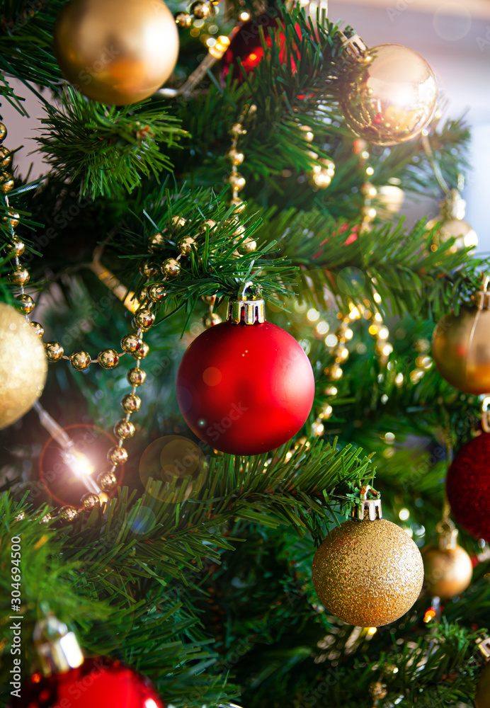 Fototapeta premium red christmas ball hanging on green pine with red and gold ornaments and lights