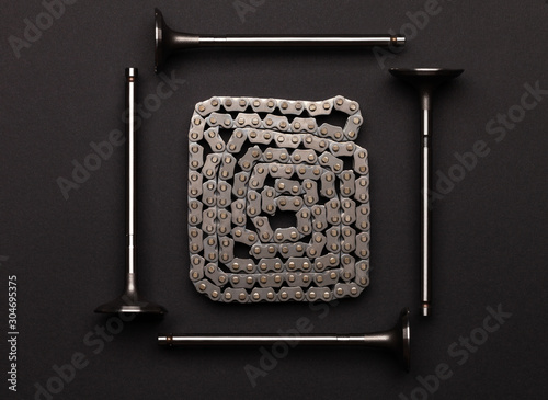 Studio photography - four gas distribution valves lie in a square, surrounding a gas distribution chain, rolled up by a snake, on a flat surface isolated on a black background.