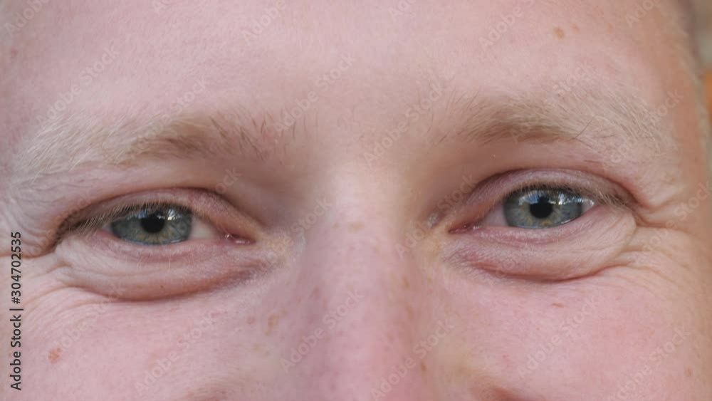 Detail view blue eyes of man staring and blinking with happy sight. Portrait of male face looking into camera with positive emotions. Facial expression of smiling young guy. Close up Detail view blue eyes of man staring and blinking with happy sight. Portrait of male face looking into camera with positive emotions. Facial expression of smiling young guy. Close up