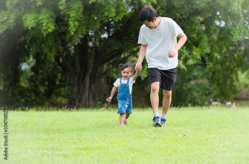Asian father and daughter are running together on the green field with full of happiness moment, concept of love and relation in family life, selective focus photograph.
