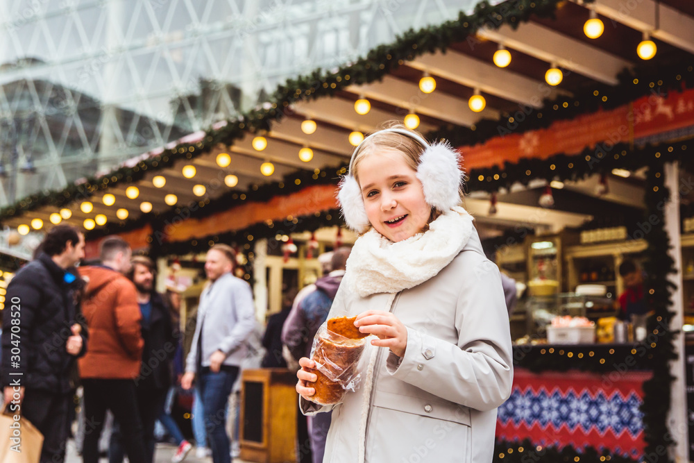 A cute little girl eats a traditional Hungarian sweet pastry called Kurtoskalacs in Budapest on the street market at wintertime