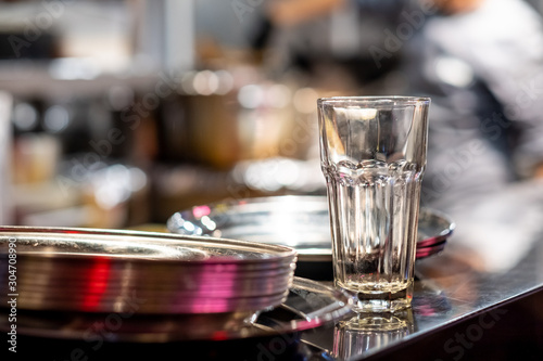 A tall empty glass water glass and a stack of plates on a table in a restaurant. Heavily blurred background