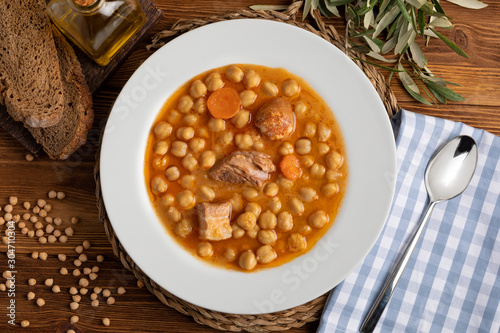 Chickpea stew dish (potage - cocido madrileño). With beef, sausage (chorizo), bacon, carrots and olive oil. Rustic appearance. Top view. photo