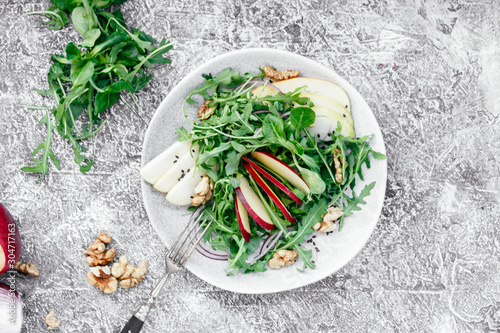 Vegetarian salad of fresh apples with arugula, onions and nuts in a plate on the table