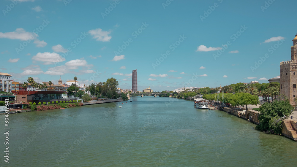 Fototapeta premium Views of the city from the bridge Puente San Telmo over Guadalquivir river towards watchtower Torre del Oro, Triana bridge and neighborhood and Cajasol Tower, in Seville, Andalusia, Spain