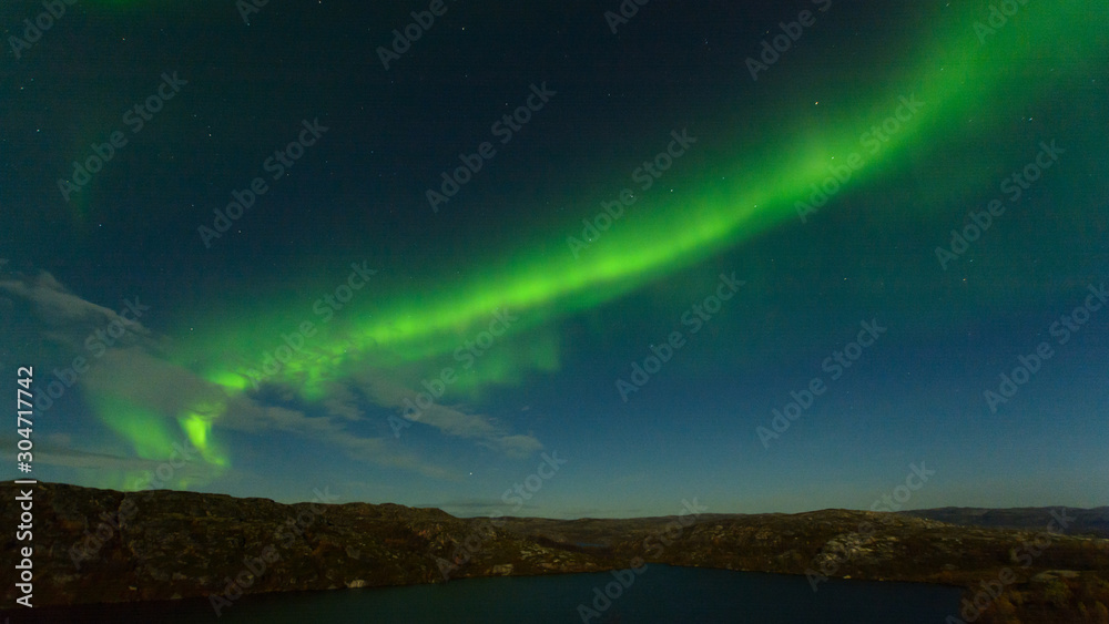 Northern lights, aurora in the sky above the hills and rocks at night.