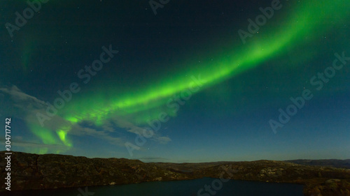 Northern lights, aurora in the sky above the hills and rocks at night. © Moroshka