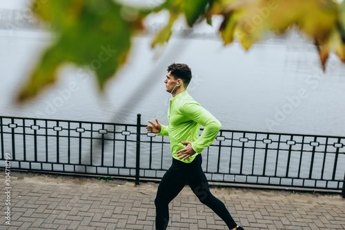 Horizontal top view image of young runner man running in the morning on the fog lake background. Fitness male exercising in the park and listenting the music on earphones. People and sport concept photo