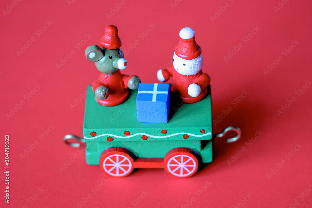 Green festive wooden train car or carriage on red background. Christmas and New Year toy with figures of mouse or rat, gnome and gift box. Greeting card, poster template Green festive wooden train car or carriage on red background. Christmas and New Year toy with figures of mouse or rat, gnome and gift box. Greeting card, poster template