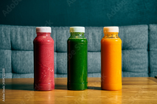 Different smoothies in bottles. Set of cherries, spinach and orange smoothie on a wooden background. Detox, healthy drink
