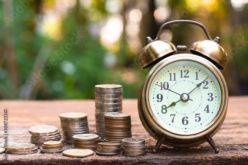 Vintage golden alarm clock with stacks of coin. Time and money for financial concept.