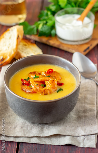 Cheese cream soup with grilled shrimp on a wooden background.