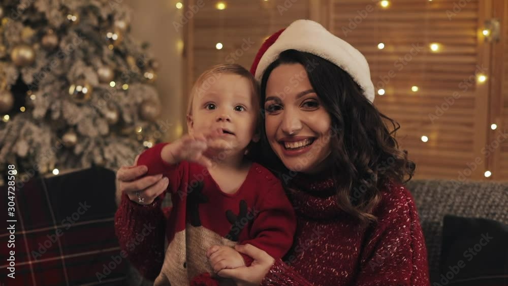 Christmas time. Happy young mother and son looking at you posing into the camera sitting on a couch in the living room at home. Christmas and new year concept. Christmas time. Happy young mother and son looking at you posing into the camera sitting on a couch in the living room at home. Christmas and new year concept.
