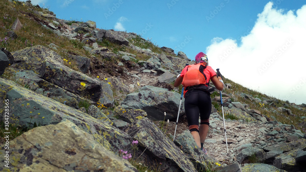 Woman skyrunner hiking in the mountains with nordic walking poles and backpacker.