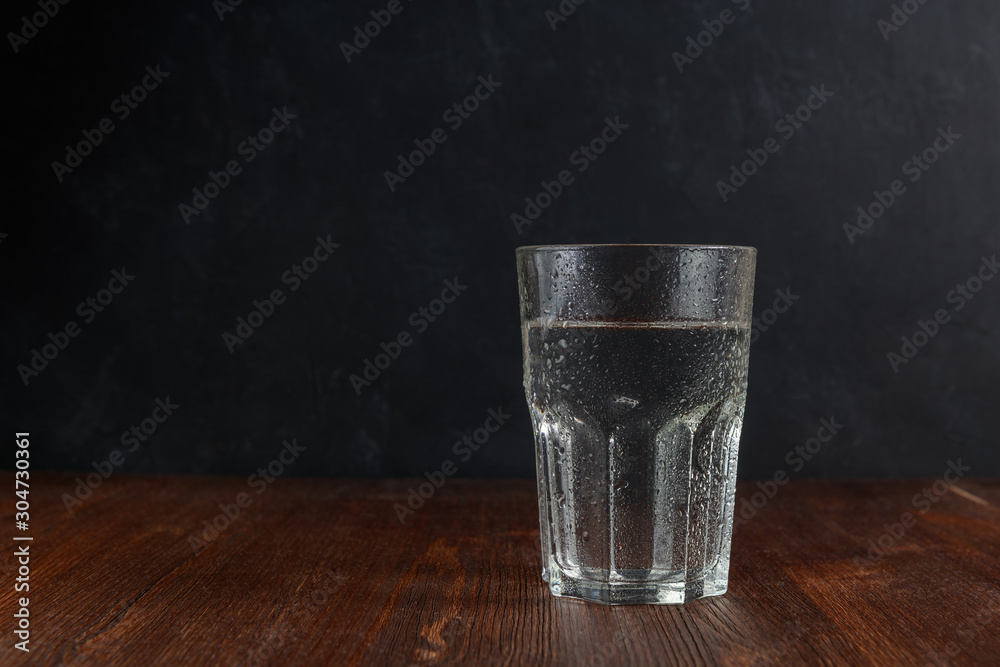 Glass of water with water drops on a wooden table with dark background. With copy space. - obrazy, fototapety, plakaty 