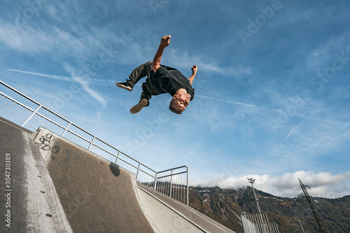 Young Parkour and Freerunning athlet doing a backflip from a wall in an urban enviroment with a blue sky in de background, jumping tumbling  Gymnastics training concept