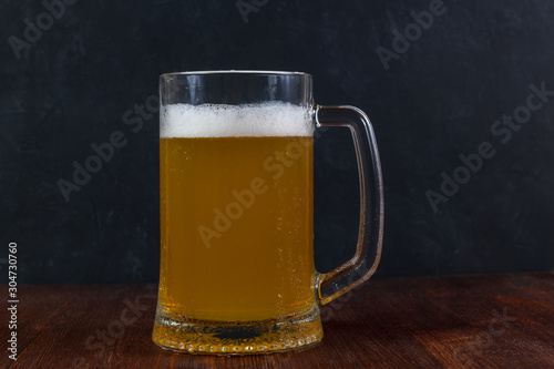 Beer in a mug with water drops on wooden table on dark background.