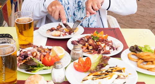 A senior woman eating an octopus with potatoes made in the Canarian style. Healthy eating. Different kind of fish on the table. Gold beer