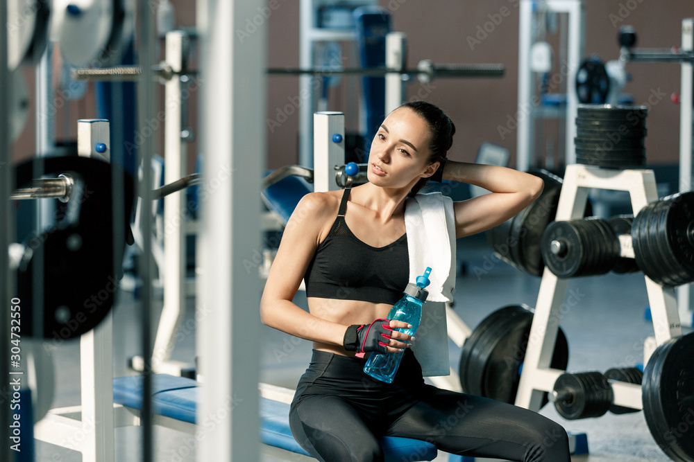 Fototapeta premium Lifestyle portrait of a young sporty woman drinking water from blue bottle in a fitness studio