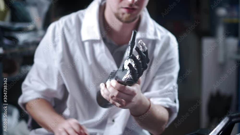 A scientist engineer is testing an electronic bionic prosthetic arm. He moves the plastic fingers of a mechanical arm. Modern technologies in prosthetics. Cybernetic hand in the hand of a scientist. A scientist engineer is testing an electronic bionic prosthetic arm. He moves the plastic fingers of a mechanical arm. Modern technologies in prosthetics. Cybernetic hand in the hand of a scientist.