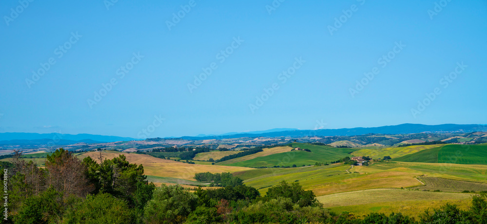 View of a sunny day in the Italian rural landscape. Unique Tuscany landscape in summer time. Wave hills, colorful fields, cypresses trees and sky.