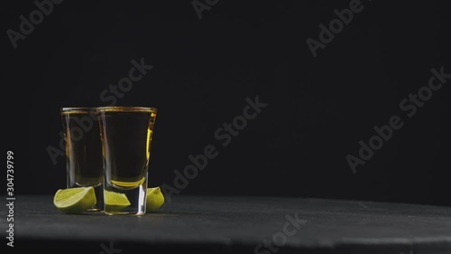 two glasses with golden tequila on a black background on a rotating black board. Coarse salt falls on top of tequila. alcoholic drinks at the bar. Close-up shot. 4k video. 59.94 fps