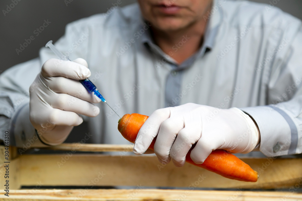 Chemical processing of vegetables, fertilizers and GMOs. A man injects chemicals into carrots