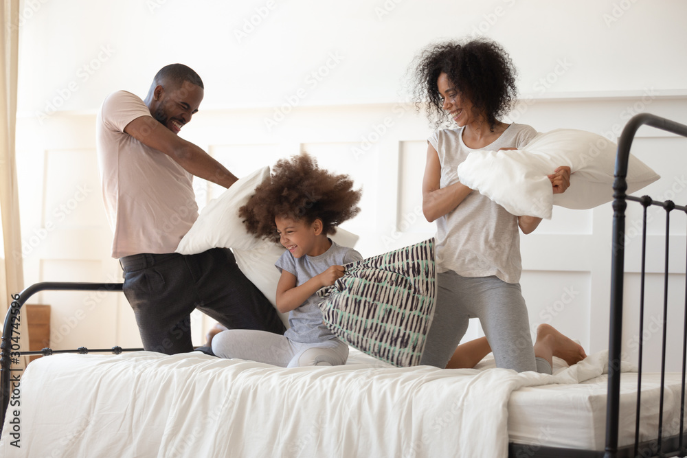 Happy biracial family with daughter have pillow fight in bedroom Happy biracial family with daughter have pillow fight in bedroom